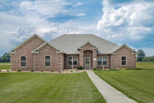 view of front of house with brick siding, a front yard, and roof with shingles