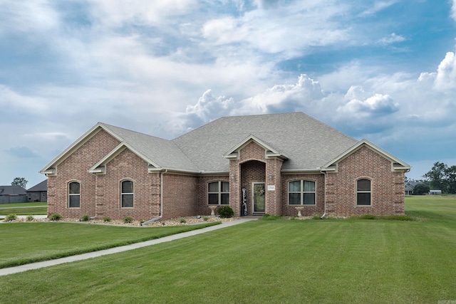 view of front facade with brick siding, a front yard, and roof with shingles