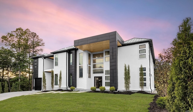 contemporary home featuring a standing seam roof, a front yard, concrete driveway, metal roof, and stucco siding