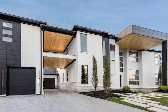 contemporary home featuring stucco siding, an attached garage, driveway, and stone siding