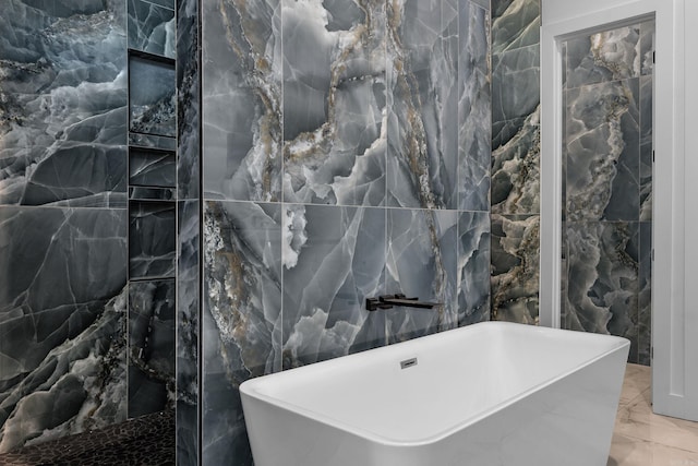 bathroom featuring marble tiled flooring, tile walls, and a soaking tub