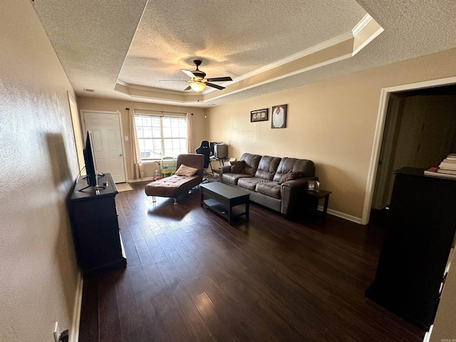 living area with a tray ceiling, a textured ceiling, ceiling fan, dark wood finished floors, and baseboards
