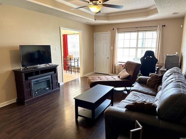living room featuring a tray ceiling, ceiling fan, ornamental molding, dark wood finished floors, and baseboards