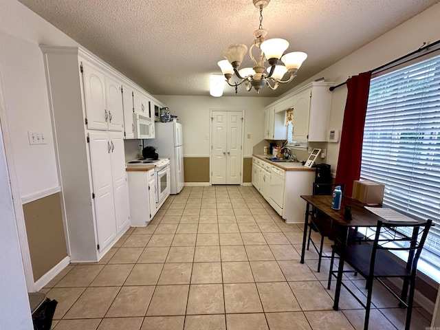 kitchen with white appliances, a chandelier, a sink, white cabinets, and a textured ceiling