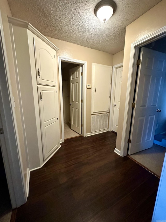 hallway featuring dark wood-type flooring, a textured ceiling, and baseboards