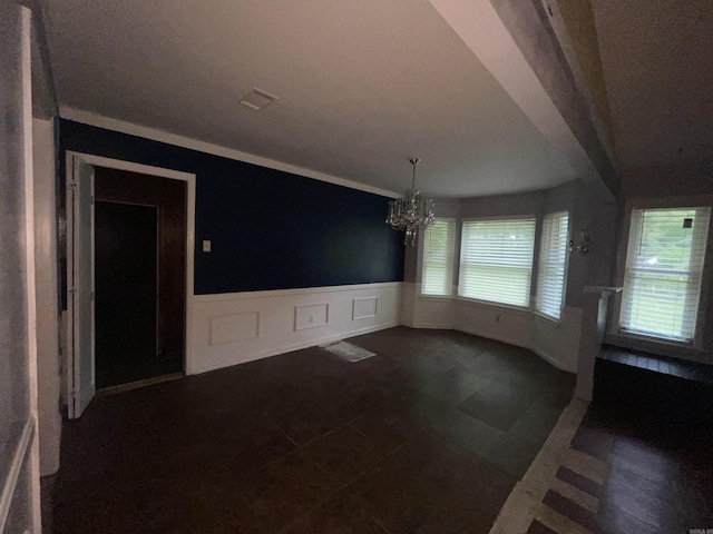 unfurnished dining area with a chandelier, a wainscoted wall, crown molding, and a decorative wall