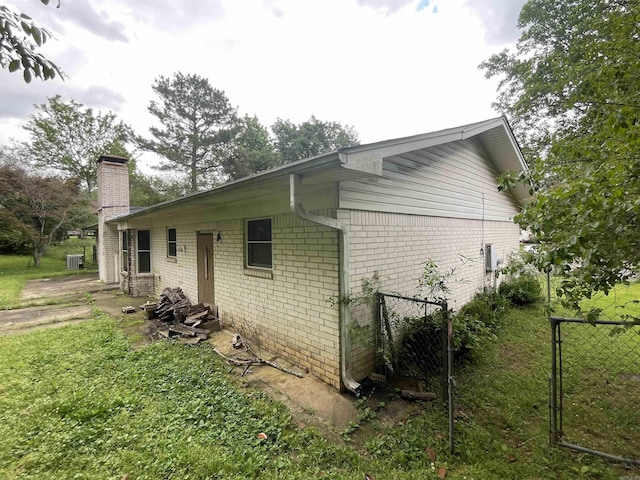 view of property exterior with a chimney, brick siding, and fence