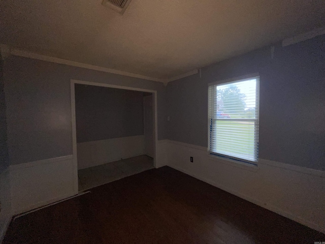 spare room with wainscoting, ornamental molding, and dark wood-type flooring