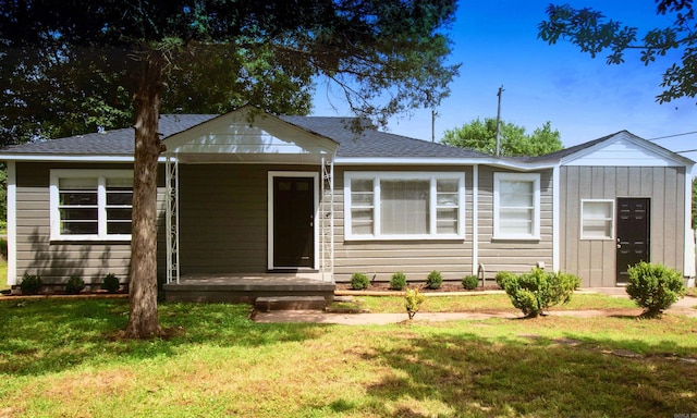 view of front facade featuring a front yard, a shingled roof, and a porch