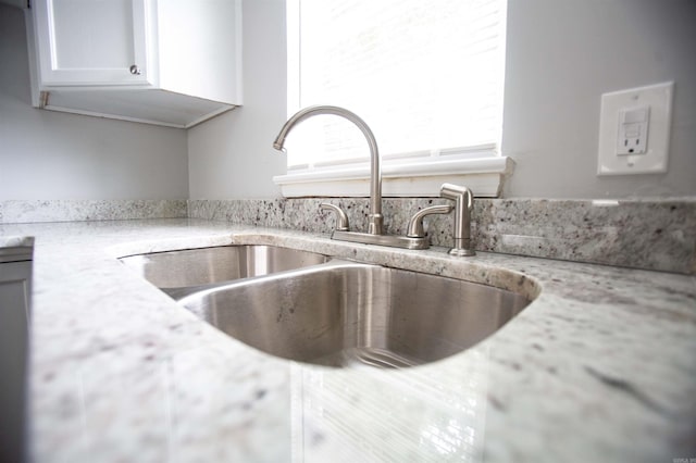kitchen view of a sink, white cabinets, and light stone countertops