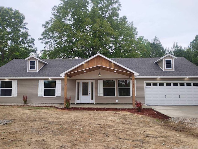 view of front of house with roof with shingles, an attached garage, concrete driveway, and covered porch