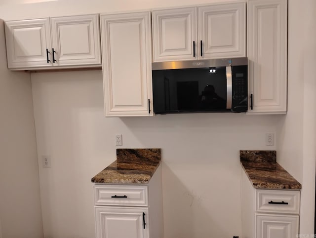 kitchen with stainless steel microwave, white cabinets, and dark stone counters
