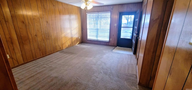 carpeted spare room with a ceiling fan and wooden walls