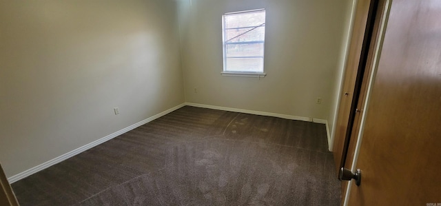 empty room featuring dark carpet and baseboards