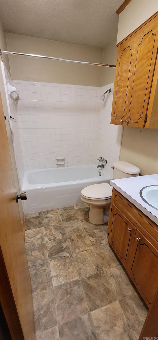 bathroom featuring toilet, washtub / shower combination, vanity, a textured ceiling, and stone finish floors