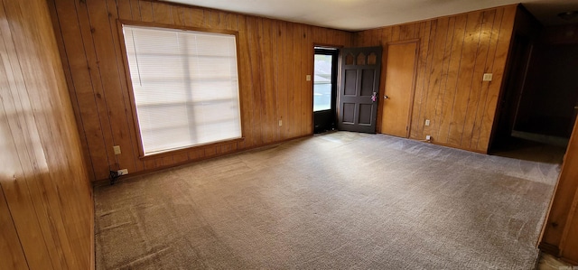 unfurnished room featuring wooden walls and carpet floors