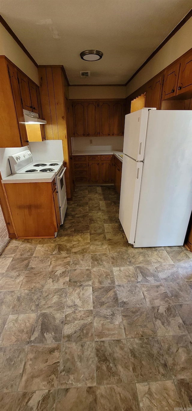kitchen with white appliances, under cabinet range hood, ornamental molding, brown cabinetry, and stone finish flooring