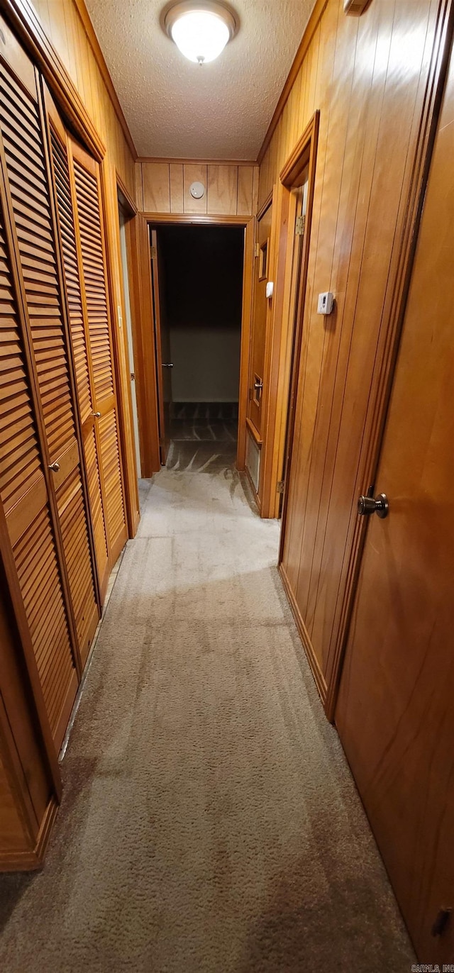 corridor featuring a textured ceiling, light colored carpet, wooden walls, and crown molding