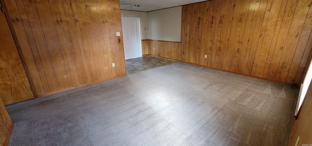unfurnished room featuring wood walls, carpet, and baseboards
