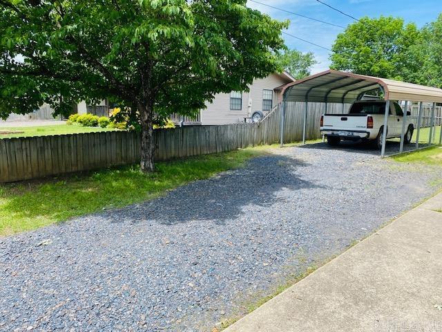 view of parking featuring gravel driveway, fence, and a detached carport