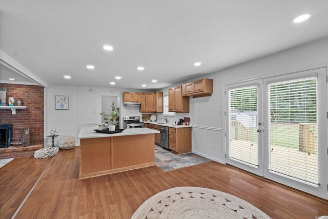 kitchen with stainless steel appliances, light wood-style floors, light countertops, a kitchen island, and a fireplace