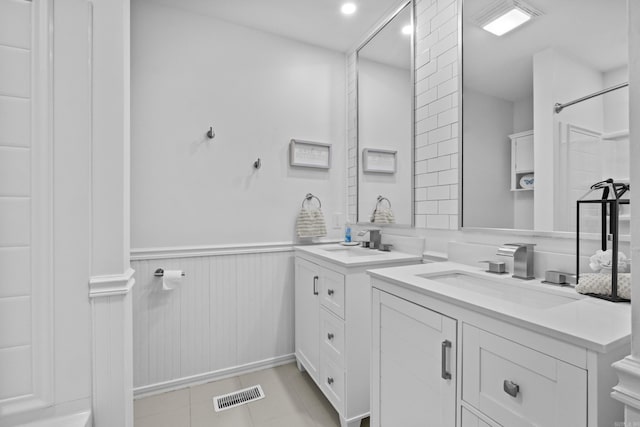 bathroom featuring two vanities, wainscoting, and tile patterned floors