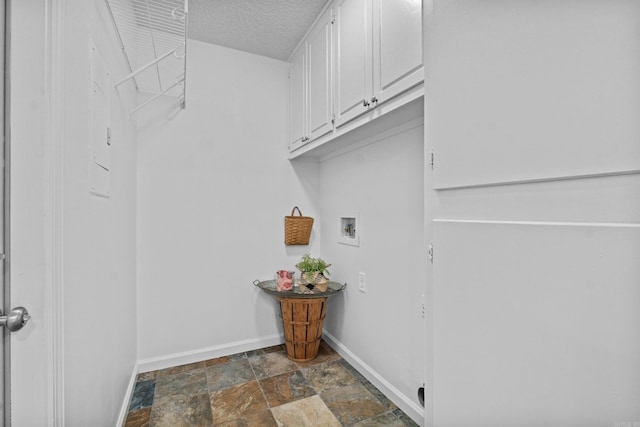 washroom featuring washer hookup, baseboards, stone finish flooring, a textured ceiling, and cabinet space