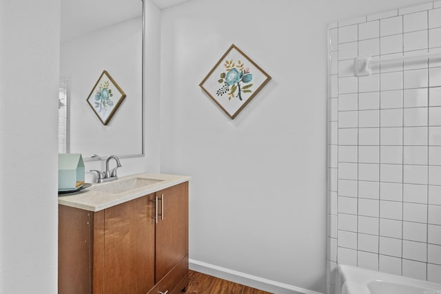 bathroom featuring wood finished floors, vanity, baseboards, and bathtub / shower combination