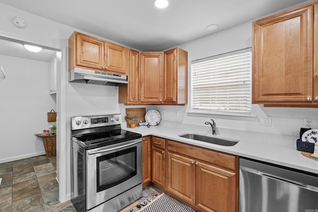 kitchen featuring stainless steel appliances, under cabinet range hood, a sink, light countertops, and dark stone finish floors