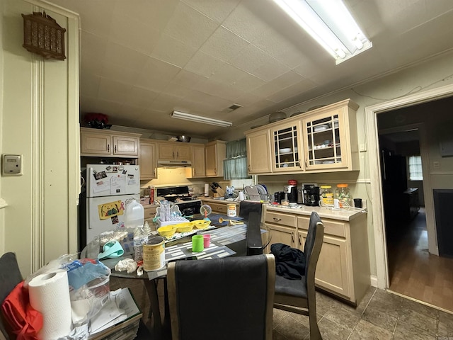 kitchen featuring freestanding refrigerator, stove, under cabinet range hood, light countertops, and glass insert cabinets