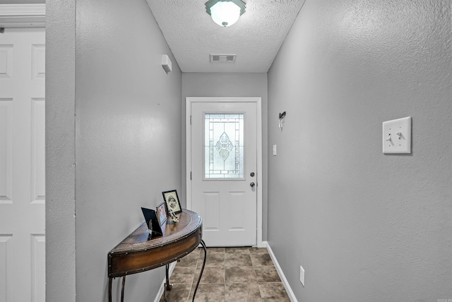 doorway featuring a textured ceiling, baseboards, and a textured wall