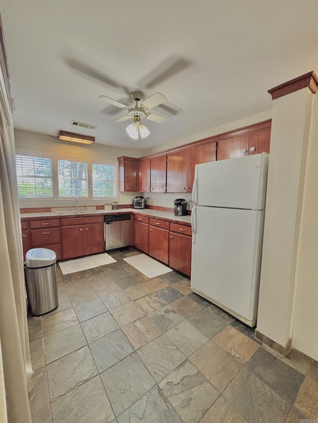 kitchen featuring freestanding refrigerator, dishwasher, a sink, stone tile flooring, and light countertops