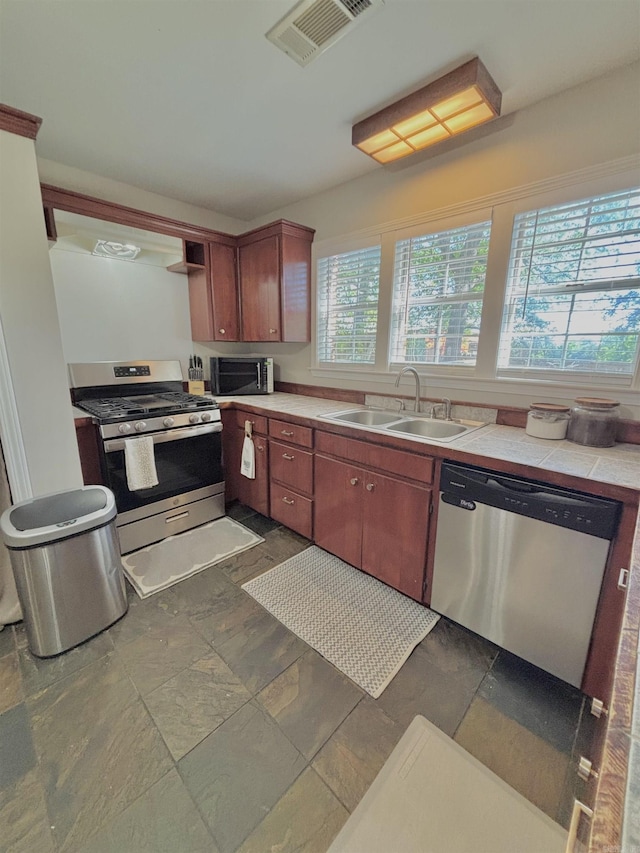 kitchen featuring appliances with stainless steel finishes, a sink, tile counters, and dark stone finish floors