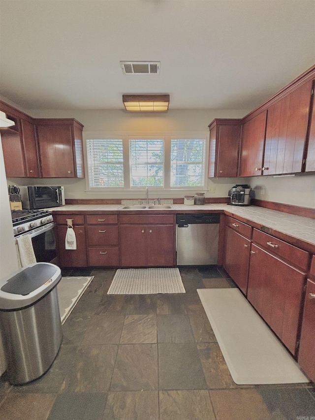 kitchen featuring appliances with stainless steel finishes, a sink, healthy amount of natural light, and dark stone finish flooring