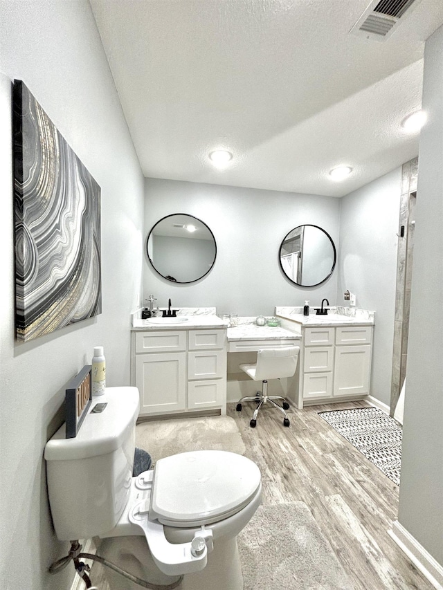 bathroom with wood finished floors, toilet, a textured ceiling, vanity, and a shower