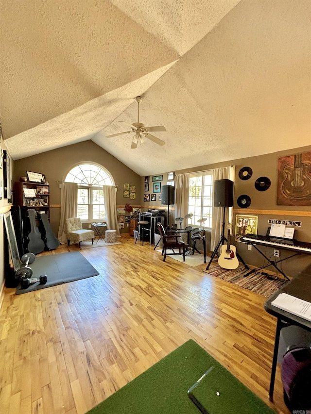 living area featuring a textured ceiling, wood finished floors, a ceiling fan, vaulted ceiling, and plenty of natural light