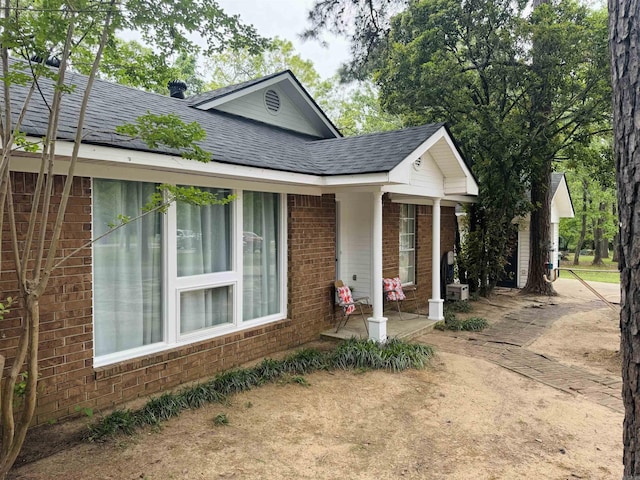 ranch-style house featuring brick siding, roof with shingles, and covered porch