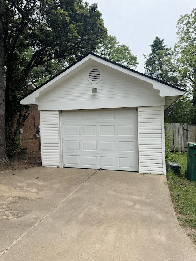 detached garage featuring concrete driveway and fence
