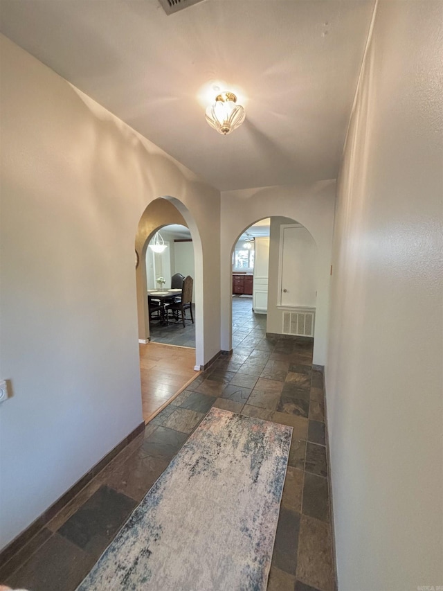 corridor with stone tile flooring, arched walkways, and baseboards