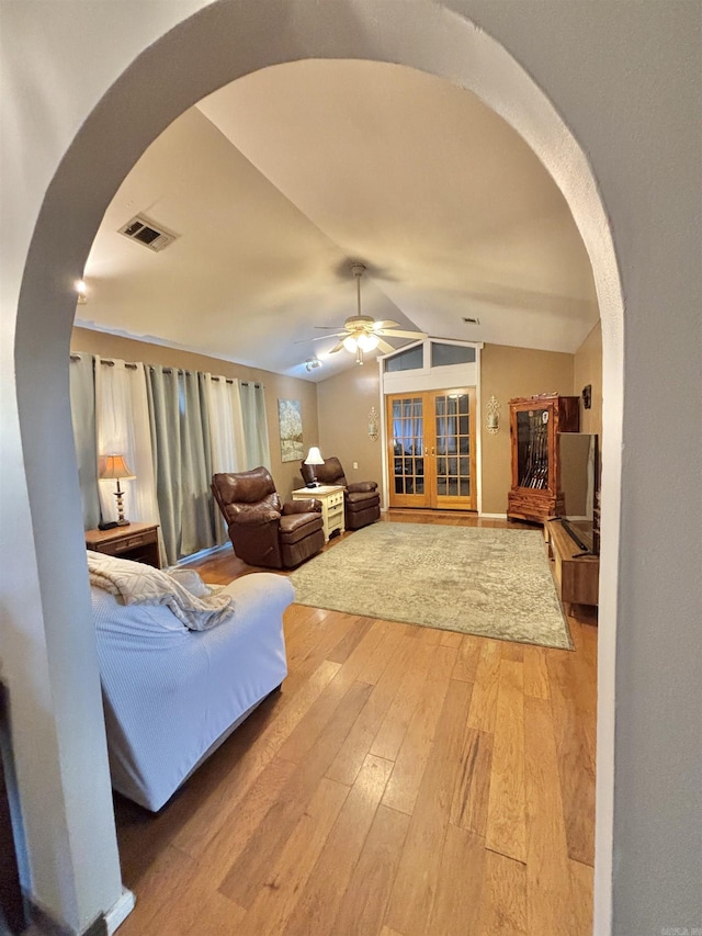 living area featuring arched walkways, light wood-style floors, lofted ceiling, a ceiling fan, and french doors