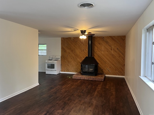 1302 Collins Dr, Pine Bluff, AR 71601 - unfurnished living room featuring wood walls, baseboards, dark wood-style floors, ceiling fan, and a wood stove
