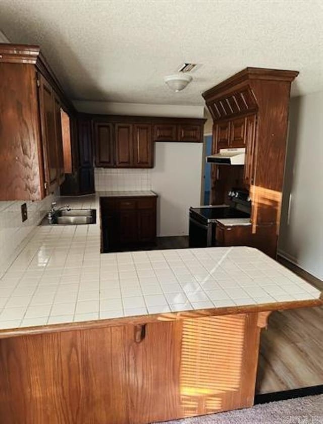 kitchen featuring black range with electric stovetop, tile countertops, a peninsula, a sink, and a textured ceiling