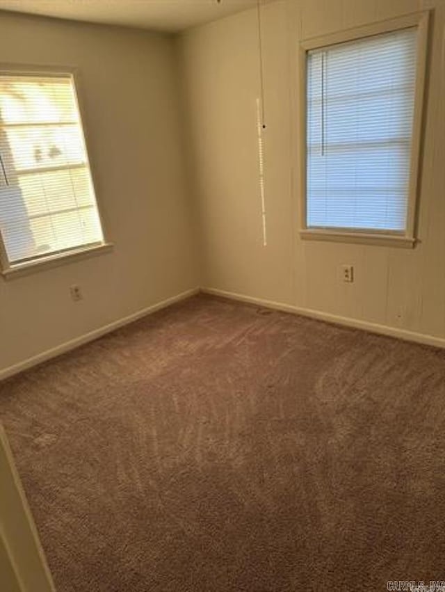 spare room featuring dark colored carpet and baseboards