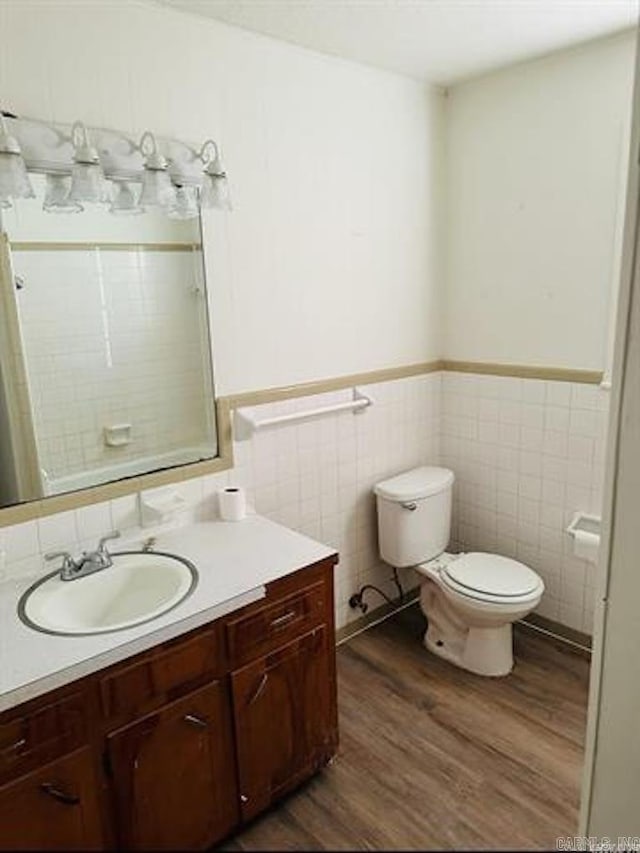 full bath featuring wood finished floors, tile walls, toilet, wainscoting, and vanity