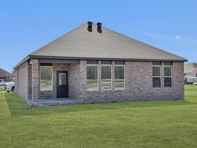 back of property with a yard, a shingled roof, and brick siding