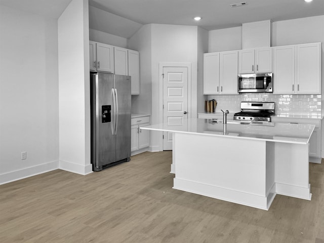 kitchen featuring appliances with stainless steel finishes, light countertops, decorative backsplash, baseboards, and a center island with sink
