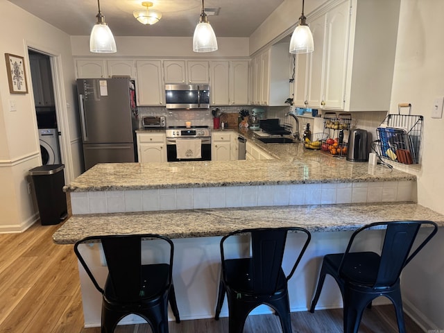 kitchen featuring stainless steel appliances, a peninsula, a sink, washer / dryer, and white cabinetry