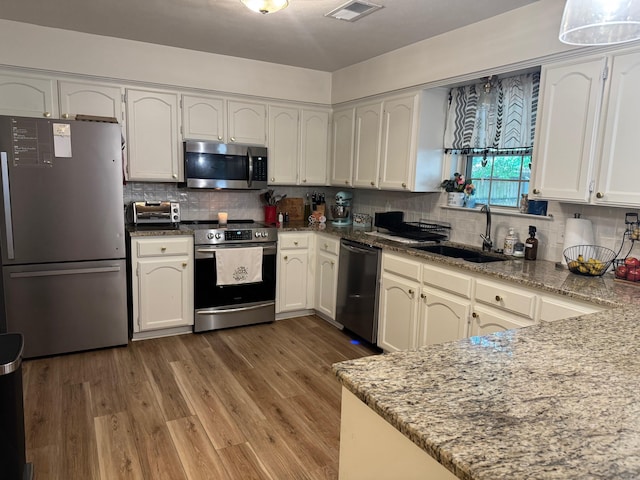 kitchen featuring appliances with stainless steel finishes, a sink, stone counters, backsplash, and white cabinets