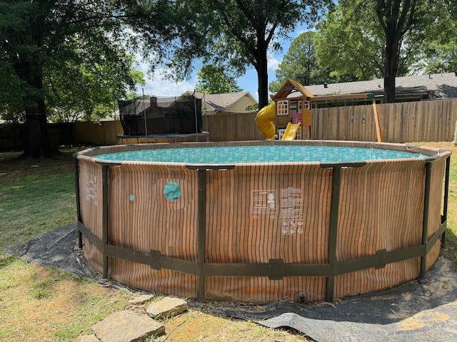 view of swimming pool with a trampoline, a fenced backyard, and a playground