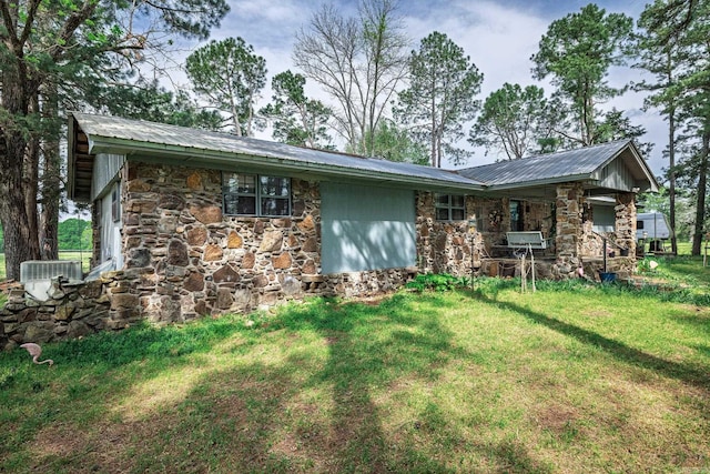 view of front facade featuring stone siding, a front lawn, metal roof, and central AC
